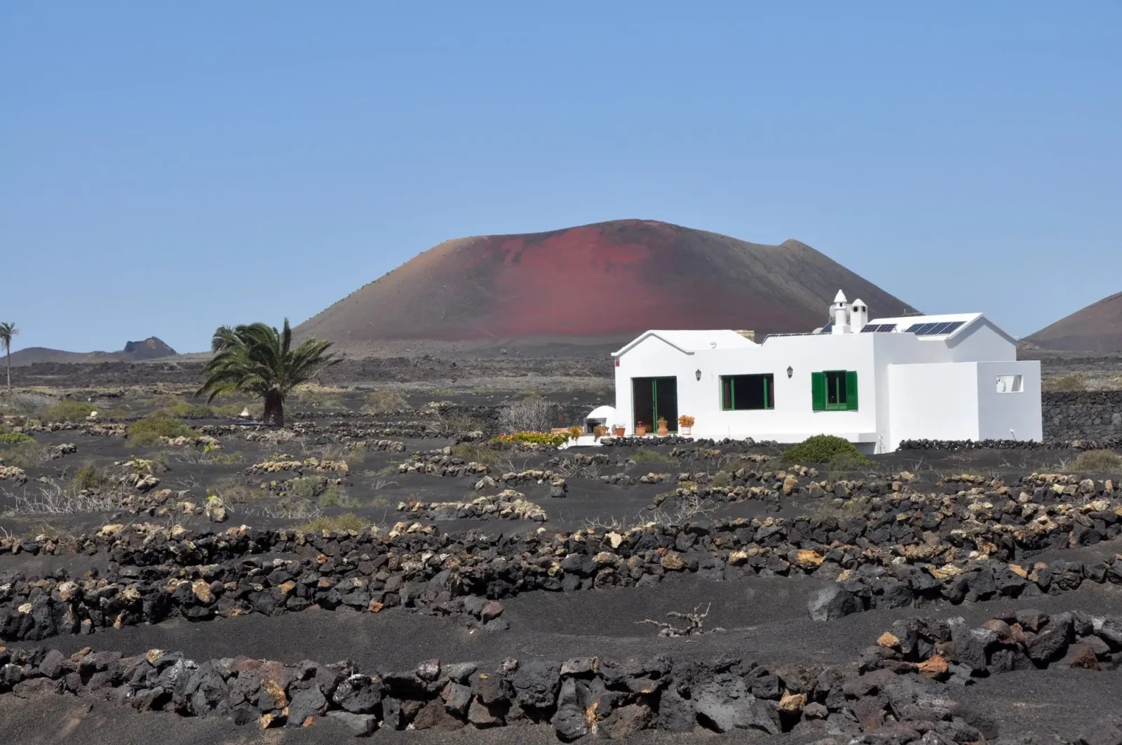 Tradiční bílý dům v sopečné krajině s červeným vulkánem na ostrově Lanzarote